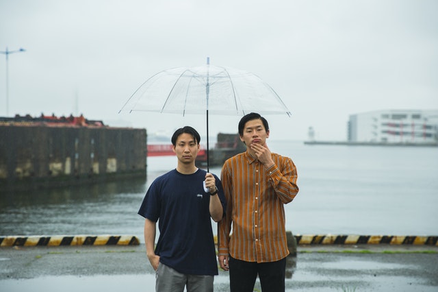 Two guys under an umbrella under the rain.